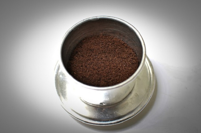 Cho bột cà phê vào phin rồi lắc nhẹ để cà phê dàn đều ra